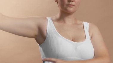 Beyaz bluzlu, beyaz elbiseli beyaz bir kız koltuk altına deodorant sıkmak için elini kaldırdı. Bej arka planda yavaş çekim stüdyosu videosu.