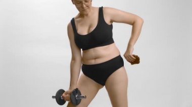 Çekici, tam şekilli, beyaz tenli genç bir kadın kurabiye yerken halterle egzersiz yapıyor. Yavaş çekim stüdyo beyaz arkaplan.