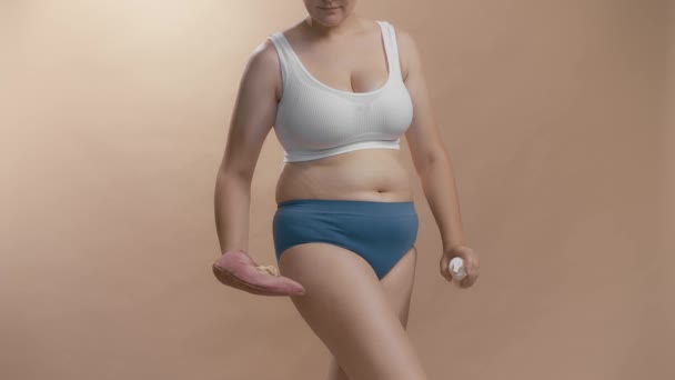 Young full-figured anonymous caucasian woman applying self-tanner to look beautiful with no sunbathing. Studio cowboy shot beige background video. — 비디오