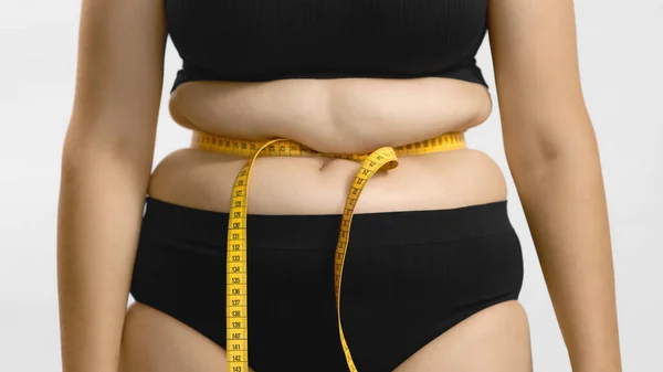 Товста жінка з проблемами ожиріння обгортає міру стрічки навколо її жирної талії. Все ще знімали високоякісні фото . Стокове Зображення