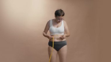 İç çamaşırlı, beyaz kadın, kendi tarzındaki başarısından ve kutlamalarından çok memnun. Bej rengi stüdyo arka planı yüksek kaliteli video.
