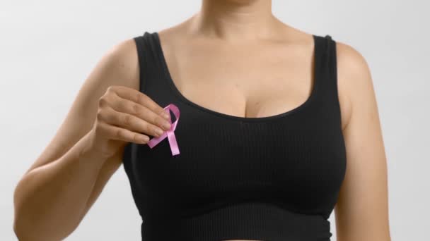 Běloška v černé bezešvé podprsence dala růžovou stuhu na rakovinu prsu. Studio anonymní střední snímek na bílém pozadí. — Stock video