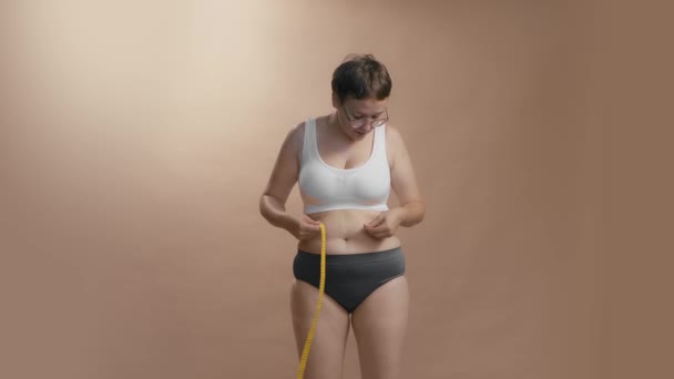 Full figured caucasian woman in underwear is very happy with her form achievement and celebrating. Beige studio background high quality video. — Vídeo de stock