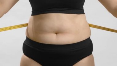 Obezite sorunu olan şişman bir kadın, şişman beline şerit takıyor. Yine de yüksek kaliteli video..