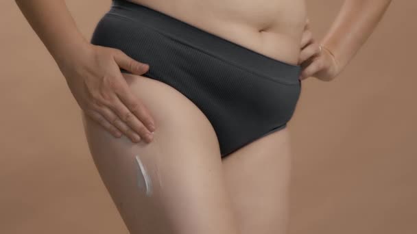 Donna caucasica a figura intera in biancheria intima mettere crema sulla gamba e massaggio. Beige studio sfondo video di alta qualità. — Video Stock