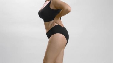 Tombul vücutlu, siyah iç çamaşırlı beyaz kız vücuduna dokunuyor ve onu takdir ediyor. Beyaz stüdyo arka planı yüksek kaliteli video.