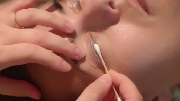 Terapeuta de beleza limpando cílios oculares de uma jovem caucasiana durante o procedimento de laminação. Extrema close-up de alta qualidade de imagens de vídeo. — Vídeo de Stock