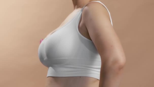 Beyaz bluzlu beyaz bir bayan göğüs kanseri için pembe kurdele işareti göstermek için etrafında dönüyor. Bej arkaplanda isimsiz stüdyo resmi. — Stok video