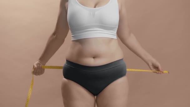 Overweight woman in underwear measuring her fat belly with measure tape. Studio still shot video. — Stock Video