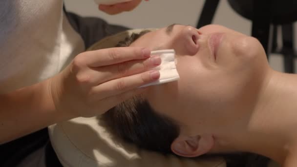 Cosmetoloog begint het gezicht van een klant voor te bereiden op wimpers lamineren procedure. Zijaanzicht videobeelden van hoge kwaliteit. — Stockvideo