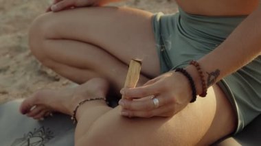 Yoga pantolonlu, Lotus pozunda oturan ve elinde palo santo sopasıyla tanınmayan beyaz bir bayan. Yakın çekim ağır çekim yüksek kaliteli video.