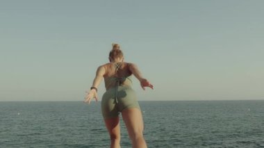 Sarışın, beyaz bir kız denizin önündeki bir uçurumda yoga yapıyor. Arka plan yavaş çekim yüksek kaliteli video görüntüleri.