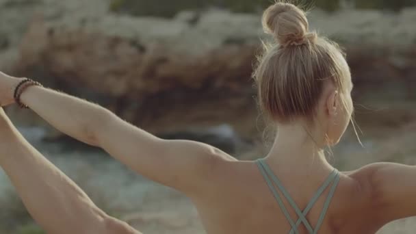 Revolved Hand to Big Toe Pose. O femeie blondă caucaziană practică yoga pe o stâncă din apropierea mării. Vedere din spate slow motion video . — Videoclip de stoc