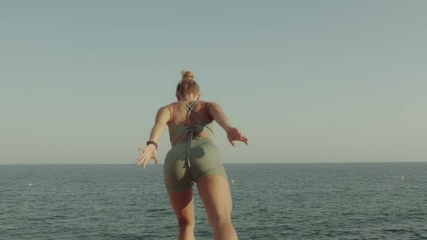 Ξανθιά νεαρή Καυκάσια που κάνει γιόγκα στον γκρεμό μπροστά στη θάλασσα. Πλάτη άποψη αργή κίνηση υψηλής ποιότητας βίντεο πλάνα. — Αρχείο Βίντεο