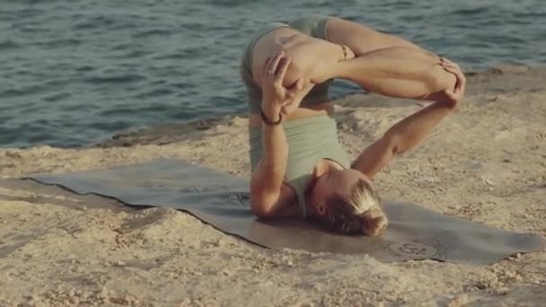 Blonďatá učitelka jógy, běloška, cvičící a zvládající obrácený lotos, pózuje na útesu před mořem. Panned slow motion video footage.