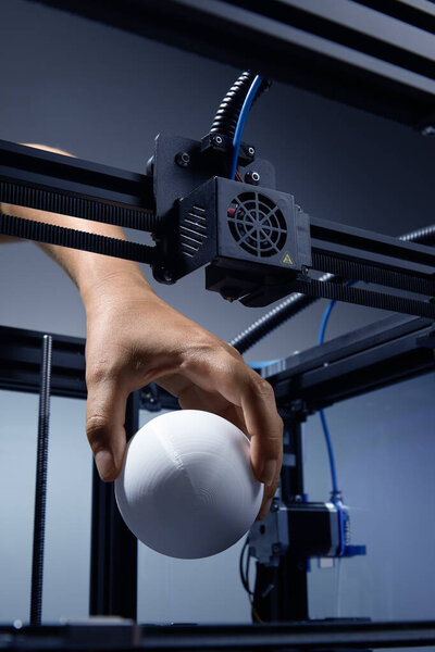 3D printer finished prototype printing. Hand lifting printed round white object. Fan, wires, tech ambient. Vertical high quality studio up view studio photo image. Royalty Free Stock Photos