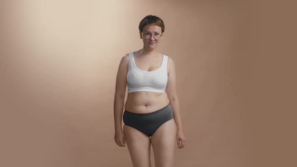 Järkyttynyt plus koko nainen katsomassa itseään puristamalla hänen vatsa rasvaa. Laadukas keskipitkällä täysi laukaus studio video. — kuvapankkivideo