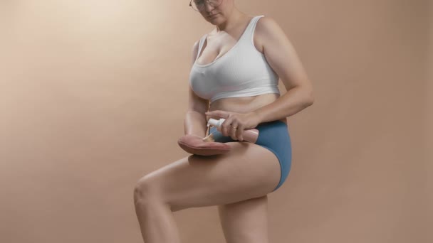 Chubby blank meisje aanbrengen zelfbruiner met een handschoen om mooi te kijken zonder zonnebad. Studio cowboy shot beige achtergrond video. — Stockvideo