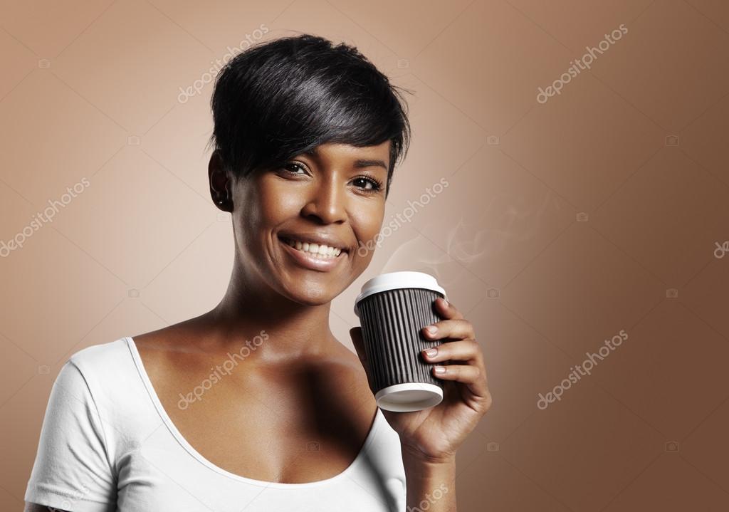 Happy black woman holding hot coffee in paper cup on brown background