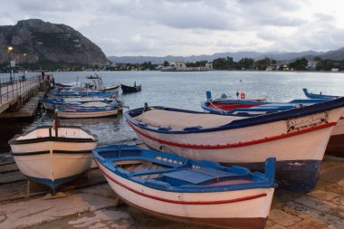 Limanda kıyıya çekilen balıkçı teknelerinin canlandırıcı görüntüsü. Arka planda demirlemiş diğer tekneler ve akşam kötü hava koşulları.