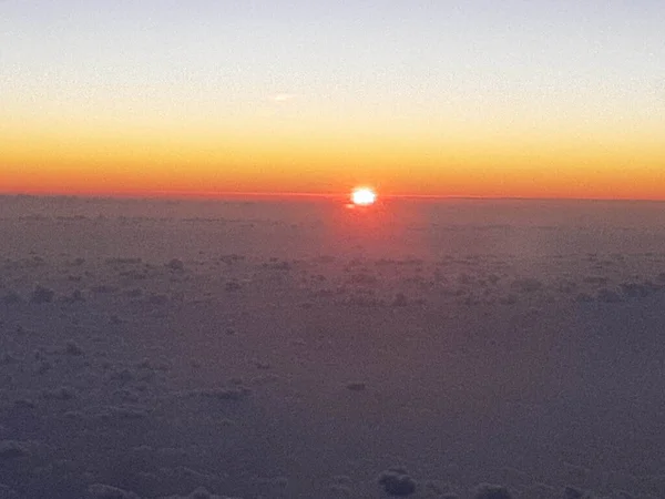 Ufukta yükselen güneş bulutlarıyla birlikte uçan bir uçaktan gün doğumunu anımsatan bir görüntü.
