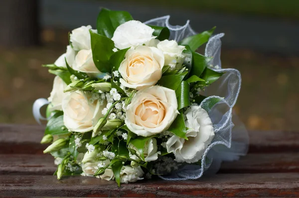 Hochzeitsstrauß aus cremefarbenen Rosen und grünen Blättern auf Holzbank — Stockfoto