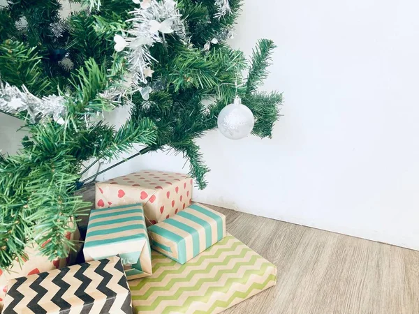 Birçok güzel renk hediye kutuları yeşil dekore edilmiş Noel ağacının altına konur. Beyaz duvar arkaplanı ve açık kahverengi ahşap zemin.