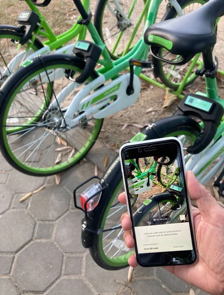 kullanıcı, halka açık parktaki yaya yoluna park eden yeşil herhangi bir tekerlek kiralama bisikleti için iPhone 'da uygulama kullanıyor