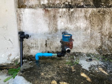 Su pompası başlığı birinin evinin önünde kırılmış. Arka fonda da eski beyaz beton çit var.