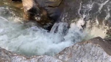 Serin şelale, gün ışığında büyük kahverengi kayaların arasına güçlü bir şekilde düşüyor. Sabah vakti, akıllı telefonlardan alınan güzel güneş ışığıyla birlikte.