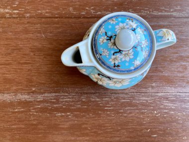 Mavi çiçek desenli Çin usulü çaydanlık koyu kahverengi masaya konmuş, yukarıdan çekilmiş.