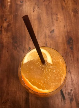Bir bardak taze buzlu portakal suyu ve kahverengi kamışlı dilimlenmiş portakal yaprağı.