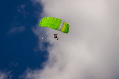 green parachute against the background of blue sky and clouds clipart