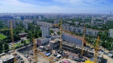 İnşaat alanının üzerinde uçuyor. Vinç raylarına monte edilmiş sarı vinçlerin üst görüntüsü. Miğferli bir ustabaşı inşaat malzemelerinin arasında yürüyor. Kazıcılar yeni bir tesis hazırlıyorlar..