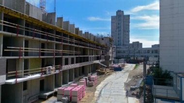 Moving along a long house under construction. Builders are installing reinforcing bars on a sunny summer day under blue sky. Building materials are along the wall. Drone footage
