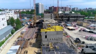 İnşaat alanının kuş bakışı görüntüsü. Kule vinçlerinin yardımıyla çitlerle çevrili bölgeye monolitik bir bina inşa ediliyor. Sarı vinç ön planda patladı. İnsansız hava aracı görüntüleri