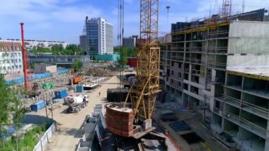 Yeni bölgenin arka planına karşı inşaat alanı manzarası. İşçiler resme beton döküyorlar. Sarı vinçler ve beton karıştırıcı kamyonlar bölgede çalışıyor. Açık sıcak hava.