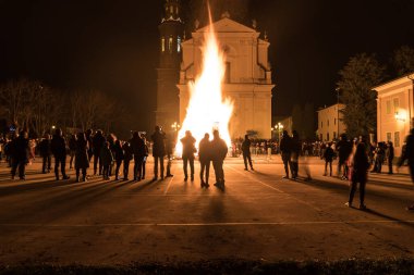 Kilise meydanında büyük bir ateşle karşı karşıya olan insanlar, güvercin fırlatan kadın şeklinde bir ateş.
