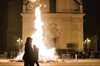 Kilise meydanında büyük bir ateşle karşı karşıya olan insanlar, güvercin fırlatan kadın şeklinde bir ateş.