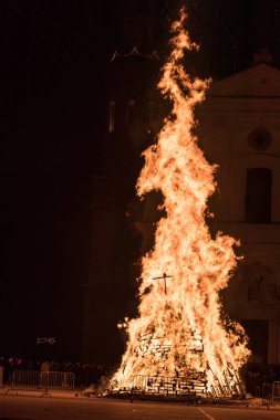 Kilise meydanında büyük bir ateşle karşı karşıya olan insanlar, güvercin fırlatan kadın şeklinde bir ateş.