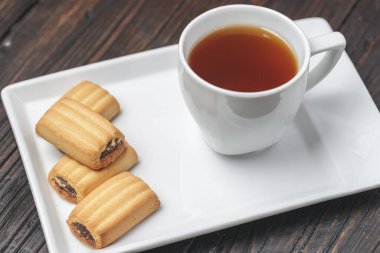 Beyaz dikdörtgen porselen tabakta çay ve kurabiye.