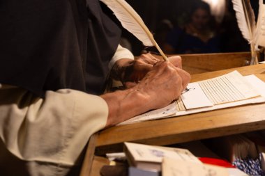 Eller kağıt üzerine yazmak için kalem kullanır. Koyu, ahşap bir yazı eğiminde..