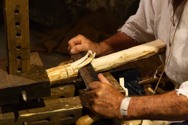 Tarihi giysiler giyen bir insan, bir çakı ya da bir ahşap parçasını ahşap mengeneye tutturmak ya da tıraş atı kullanmak zorundadır..