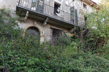 Çürüyen bir balkon, paslı bir korkuluk ve kısmen açılmış ahşap kapılar..