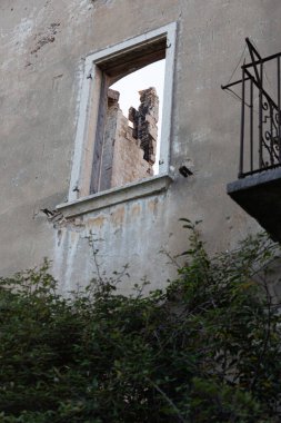 Aşırı büyümüş balkon, kemerli, parmaklıklı bir kapının üstünde boyası ve demir parmaklıkları var..