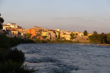 Ön planda akan bir nehir. Kıyısında güneşli bir Akdeniz kasabası var..