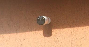 Kırmızı Duvara monte edilmiş Beyaz Kablosuz Güvenlik Kamerasının yakın plan görüntüsü.
