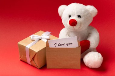 White teddy bear with hearts and gift box on red background, Valentine's day close up