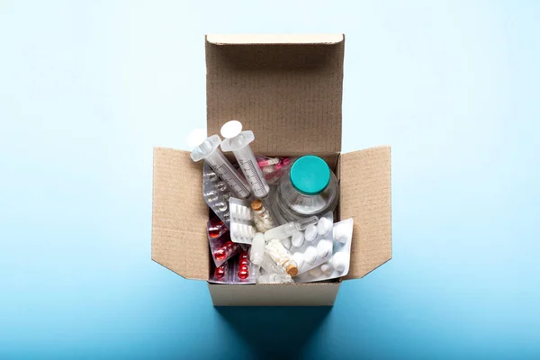 Delivery box filled with medicines and drugs from the pharmacy. Cardboard box with medicines, pills, bottles, injections isolated on blue background top view