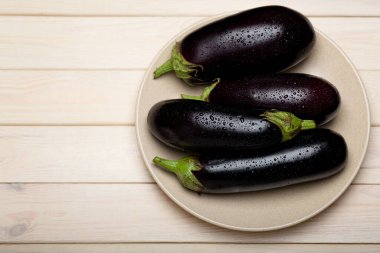 Ahşap zemin üzerinde olgun patlıcanlarla kaplı bir tabak, üst görünüm kopyalama alanı, sağlıklı beslenme arka planı